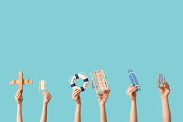 Female hands holding mini deck chairs with surfboard, plane and lifebuoy on blue background