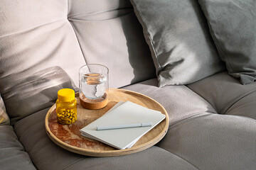 Couch with Tray Holding Medicine Bottle, Glass of Water and Notebook. Daily Routine for Health and Wellness at Home.