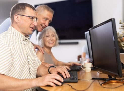 Middle-aged man sitting at computer together with other mature attendees of IT courses