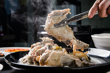 A picture of a boiled chicken being lifted with tongs
