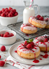 A plate of donuts with raspberry sauce and raspberries on top. The plate is on a table next to a glass of milk