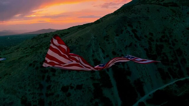 A large free flying american flag against the warm backdrop of a sunset over a Utah valley