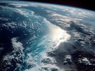 Fototapeta premium A breathtaking satellite view showcases Earth's stunning coastal landscape with a bright sunlit area reflecting off the ocean and clouds.