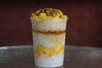 This enticing dessert features creamy layers of yogurt, rice, and fresh mango, topped with granola for a delightful sweet and crunchy finish, perfect for on-the-go enjoyment.