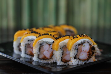 A beautifully arranged sushi platter featuring rolls topped with vibrant mango, shrimp, and delectable sauces, perfect for sushi aficionados and food enthusiasts alike.