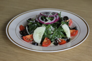 A beautifully arranged green salad featuring fresh vegetables, olives, and red onions, showcasing the art of healthy eating in an appealing and colorful way.