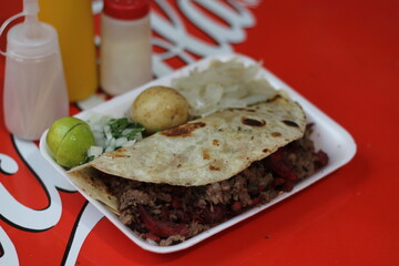 This image captures a generous taco filled with grilled carne asada accompanied by lime, onions, and condiments, emphasizing traditional Mexican culinary culture.
