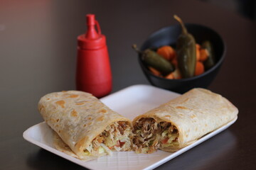 A tantalizing burrito filled with tender meat, fresh vegetables, and a hint of spice, served with jalapeños and a squeeze bottle of sauce for added flavor.