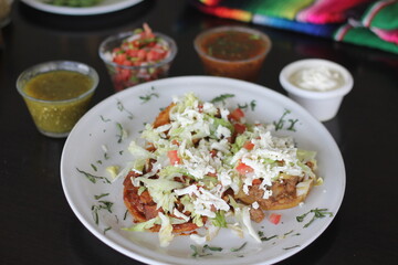 A vibrant plate of sopes topped with lettuce, cheese, and fresh salsa, showcasing the beauty and richness of traditional Mexican cuisine in a colorful presentation.