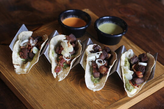 An enticing platter featuring four delicious tacos filled with savory meat and garnished with fresh ingredients, paired with vibrant sauces for an extra flavor boost.