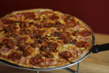 An appetizing pizza topped with pepperoni, sausage, and cheese is presented on a wooden table, showcasing its delicious and enticing appearance for food lovers.