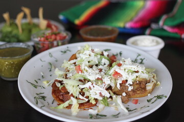 This image showcases a vibrant plate of sopes topped with lettuce, tomatoes, and cheese, accompanied by colorful salsas and guacamole, highlighting authentic Mexican cuisine.