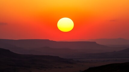 Fototapeta premium A brilliant sun sinks low over distant mountain ranges, painting the sky in vibrant hues of orange and red. A stunning landscape