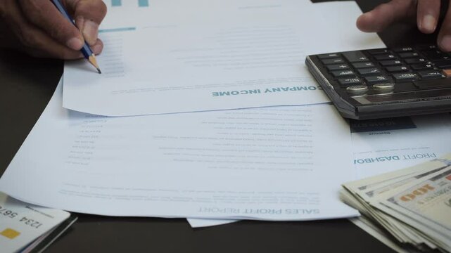 a man is calculating financial statements and matching them with several sheets of financial documents on his desk. business and financial concepts