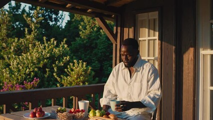 Black man enjoying breakfast on a wooden veranda at sunset - Powered by Adobe