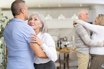 Two married couples enjoying slow dancing at a house party for friends