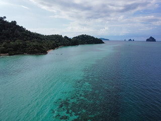 Lush green vegetation covers the hilly coastline, meeting the vibrant turquoise waters under a...