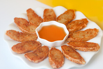 Pontianak Food. Close up of fried hekeng arranged like flower petals on a white plate, with a bowl of sweet honey sauce (kitjiu). The background blends yellow and white tones.