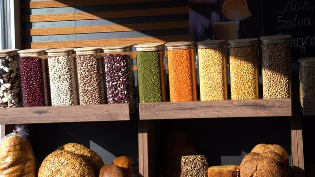 Morning sun shining across plastic bins of legumes, grains, and fresh bread displayed in market.