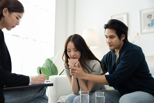Emotional Asian woman sitting in tears while partner comforts beside, expressing deep sadness and stress due to infertility, couple facing fertility challenge and seeking mental health support