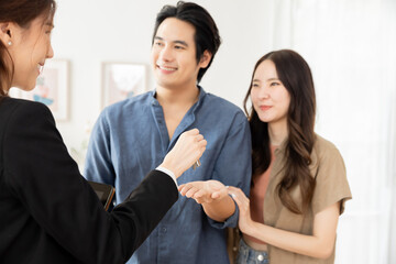 Asian man and woman smiling while receiving keys from female real estate agent, highlighting positive home buying experience, real estate success, and emotional reward of owning new property together