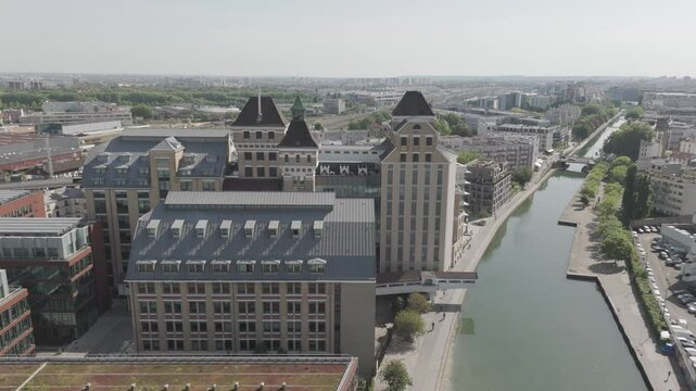 Drone shot pulling away from Grands Moulins de Pantin and canal with Paris skyline in view - France