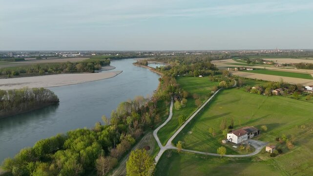 rone shot captures green rural fields, meandering river, scattered farms, and patchwork of spring crop fields under clear sky, highlighting mixed land use and agricultural textures near Isola Serafini