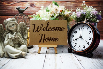 Welcome Home text on easel with alarm clock and flowers decoration on wooden background