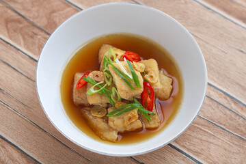 Steamed fillet fish served in a light broth, topped with sliced chili, scallions, and fried garlic. Captured on a white plate under natural light, highlighting the fresh and savory presentation.