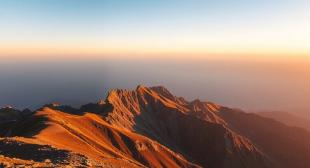 Naklejka premium Golden hour mountain landscape with warm sunlight on rugged terrain. Clear blue-to-cream sky gradient above offers ample negative space, creating a serene, scenic, and spacious visual tone.