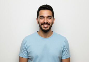Fototapeta premium A smiling young man with a beard poses in a light blue t-shirt against a white background