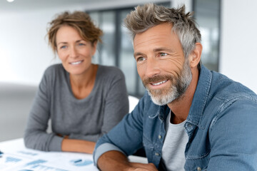 A smiling mature couple sitting together, appearing relaxed and engaged in a bright, modern office environment.