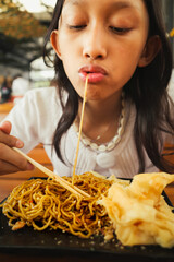 Close up portrait of an Asian teenage girl eating noodles and fried dumplings with appetite in her favorite restaurant 