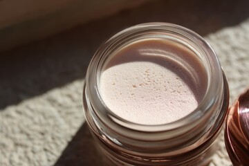 Close-up view of a light-pink cosmetic product in a glass jar.