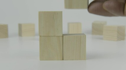 A hand places the last of four square wooden blocks next to another block on a white background, symbolizing the final steps in a sequence, nearing completion, or concluding a process in a clean and m