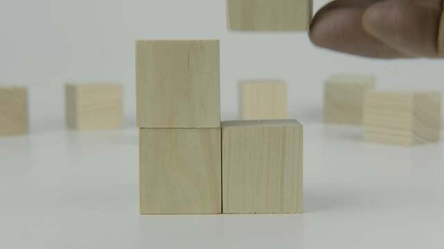 A hand places the last of four square wooden blocks next to another block on a white background, symbolizing the final steps in a sequence, nearing completion, or concluding a process in a clean and m