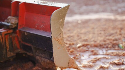 Close-up of a soil tiller blade on a muddy surface.