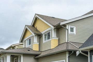 Top of grey stucco luxury house with shingle roof, green trees and nice windows in Spring in Vancouver, Canada, North America. Day time on April 2025.