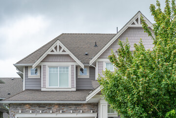 Top of grey stucco luxury house with shingle roof, green trees and nice windows in Spring in Vancouver, Canada, North America. Day time on April 2025.