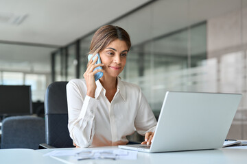 Smiling busy middle aged business woman making call on cellphone at work communicating with...