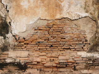 Picture of an old cement wall that has been cracked to reveal red bricks.