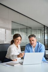 Professional bank manager consulting company client on financial taxes. Two middle aged professional executives team business people working on laptop computer at office corporate meeting. Vertical