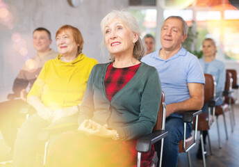 Positive interested elderly woman listening attentively and taking notes on lesson during language...
