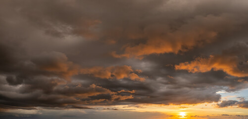 Colorful sunset sky with setting sun behind vivid orange and yellow clouds