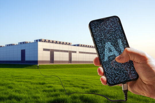 Close-up of a smartphone in hand with “AI” composed of thousands of micro-letters on screen, blurred data center in background — representing AI’s deep connection to data processing power.