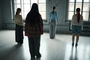 Group of four women performing dance moves and facing large windows in a bright, spacious studio....