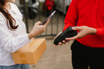 A young Asian deliveryman in uniform smiles while delivering a cardboard package to a customer’s home, ensuring safe and timely shipment.