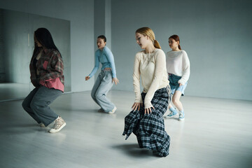 Group of young women practicing intricate choreographed dance routine in spacious studio with reflective mirror wall and natural wooden floors. Each dancer is focused on perfecting movements