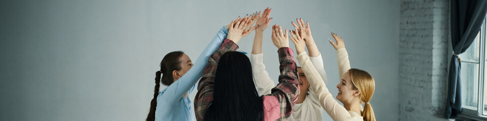 Group of diverse young women celebrating by raising hands together in gesture of unity and support...