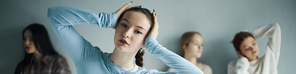 Fototapeta premium Portrait of young woman holding her head while three others are blurred in background, creating a sense of focus and depth in the composition